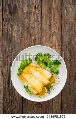 Seared halibut fillet, sliced lemon and boiled broccoli on wooden table 