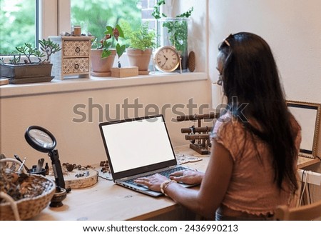 Woman works on laptop with blank screen on office desk near window. Workplace during home office. 