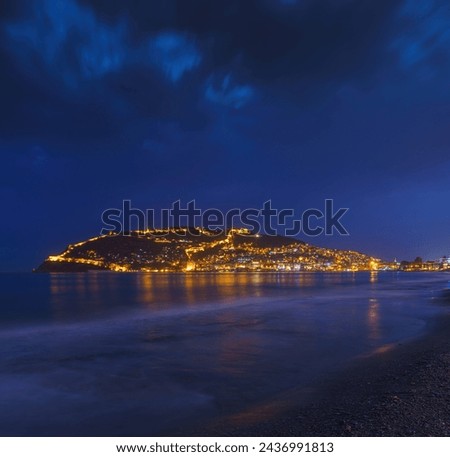 Alanya, Antalya, Türkiye, Turkey, Panoramic view of the beach, in the background a city with street lights, and a mountain with an Alanian fortress, the Mediterranean Sea, at night