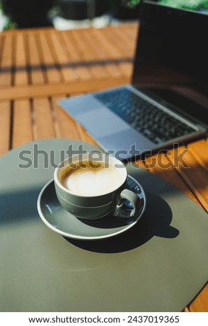 A cup of aromatic coffee on the background of a laptop on a summer terrace. Work in a cafe. Remote work online.