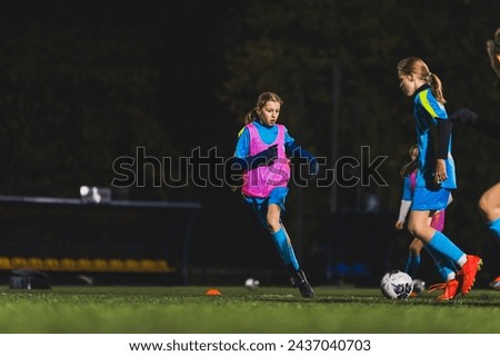 young girls in blue uniforms playing soccer on a grassy field at night, teamwork in sport. High quality photo Royalty-Free Stock Photo #2437040703