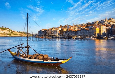 Old town of Porto, Portugal. Antique boat with port wine barrels on the water Douro River. Sunny day over silhouettes skyline roofs houses along river. Royalty-Free Stock Photo #2437053197