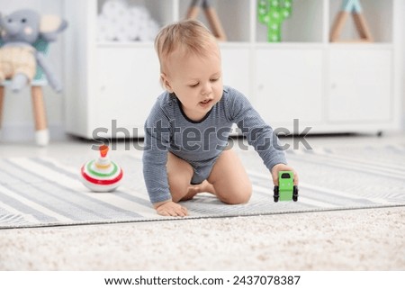 Children toys. Cute little boy playing with toy car on rug at home Royalty-Free Stock Photo #2437078387
