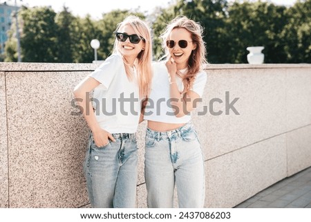 Two young beautiful smiling hipster female in trendy summer white top and jeans clothes. Carefree women posing in the street. Positive models having fun outdoors. Cheerful and happy. In sunglasses