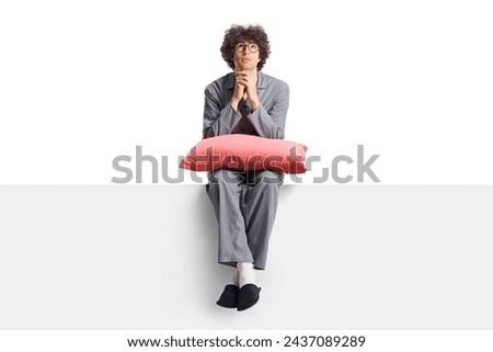 Young man in pajamas sitting on a blank panel and thinking isolated on white background