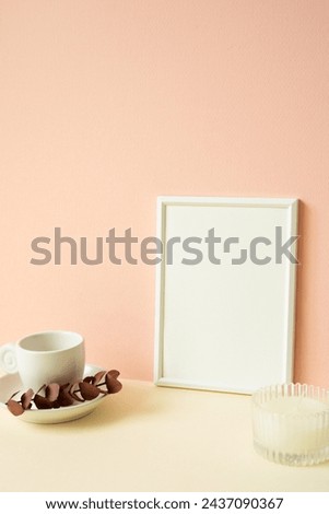 White blank picture frame with coffee cup, candle on ivory table. pink wall background