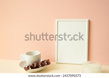 White blank picture frame with coffee cup, candle on ivory table. pink wall background