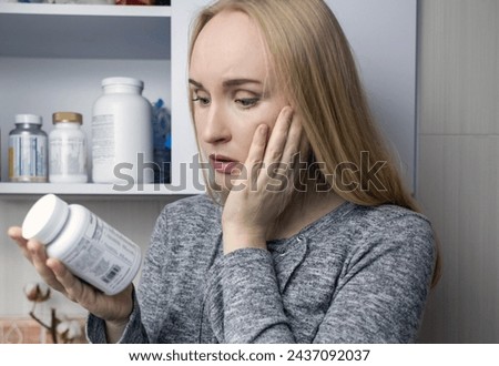 Girl studies dietary supplements. Reading the instructions on a bottle of vitamin complex. Nutritional supplement for hair loss and  weakened immunity. Self-prescription of drugs and harm to health Royalty-Free Stock Photo #2437092037