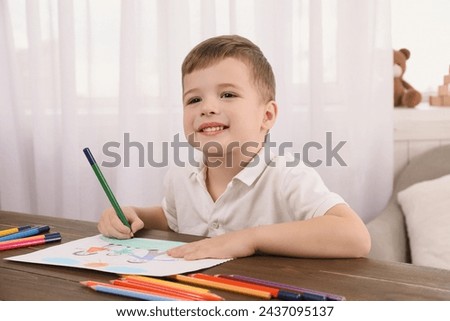 Cute little boy drawing with pencil at wooden table in room. Child`s art