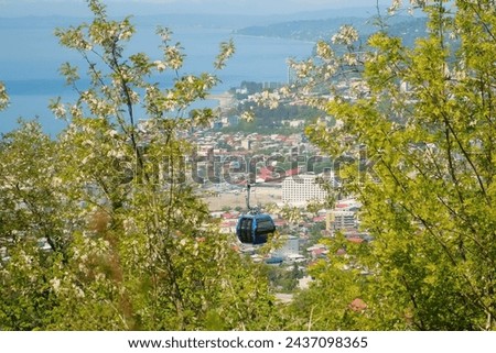 View through trees on cableway with moving funicular cabin and coastal Batumi city, Black sea from high mountains. Ropeway, cable car in Georgia. Travel, tourism, vacation, wanderlust concept. Royalty-Free Stock Photo #2437098365