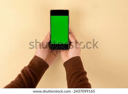 Human hands holding smartphone with green screen background.