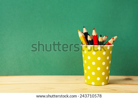 color pencils in yellow polka dot paper glass over retro green background  Royalty-Free Stock Photo #243710578