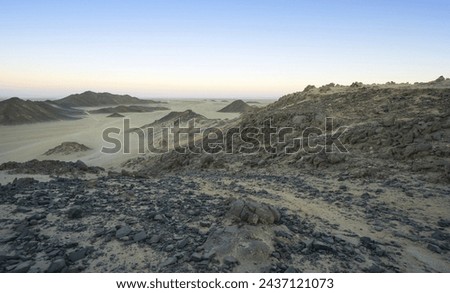 High angle and sunset view of black pebbles on the hill at Sahara Desert against mountain and land horizon, Hurghada, Egypt
