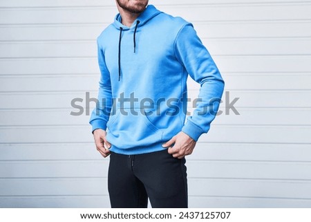 A Man in a Stylish Blue Hoodie Leans Against a White Wall. Logo and brand swag mock-up. Isolated horizontal photo.