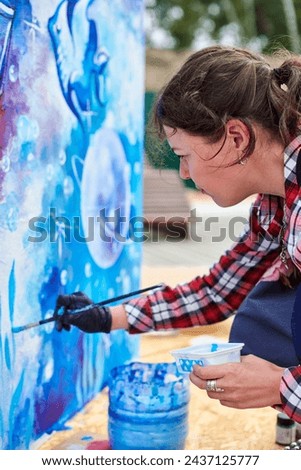 Female painter draws picture with paintbrush on canvas for outdoor street exhibition, close up side view of female artist apply brushstrokes to canvas, symphony of art creativity