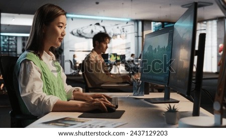 Asian Woman Using Desktop Computer And Designing In 3D Modelling Software Unique World And Characters For Survival Video Game In Diverse Office. Female Game Designer Creating Immersive Gameplay