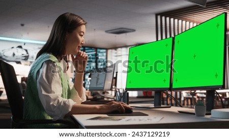 Female Asian Game Designer Using Desktop Computer With Green Screen Chromakey on Display, Designing Characters In 3D Modeling Software For Survival Video Game. Woman Working In Game Development Office