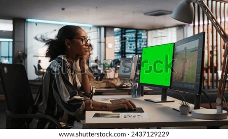 Female Black Game Designer Using Desktop Computer With Green Screen Chromakey on Display, Designing Characters In 3D Modeling Software For Survival Video Game. Woman Working In Game Development Office