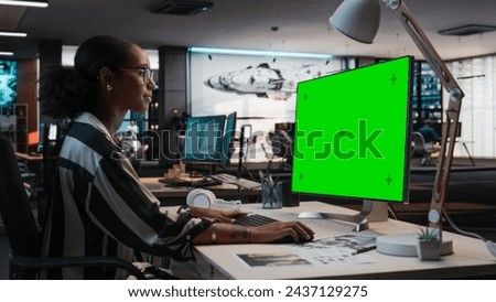 Portrait of Creative Black Female Sitting at a Desk Using Desktop Computer with Mock-up Green Screen. Female Concept Artist Working in Game Design Startup Office, Creating Immersive Gameplay.