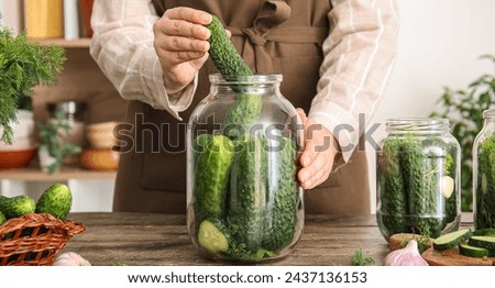 Woman preparing fresh cucumbers for canning at table in kitchen