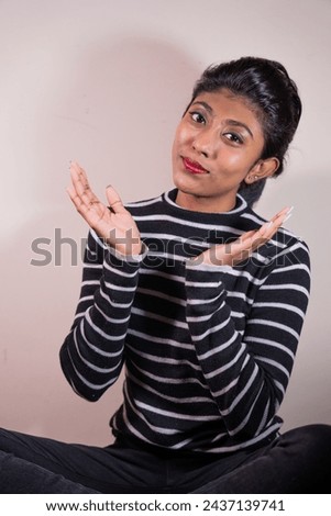 A woman in a striped shirt is sitting on the floor and making a face. She is wearing red lipstick and has her hands on her hips. Concept of casualness and nonchalance
