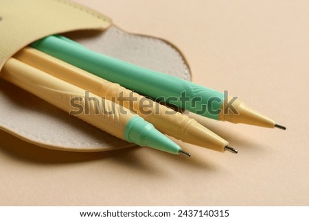 Three pens in pencil case on beige background. Closeup Royalty-Free Stock Photo #2437140315