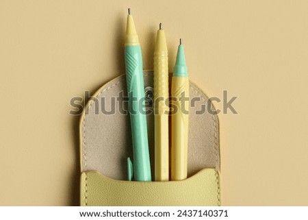 Three pens in pencil case on beige background. Top view Royalty-Free Stock Photo #2437140371