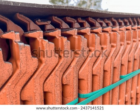 Roof tiles stacked on a pallet, visible from the side as a background.