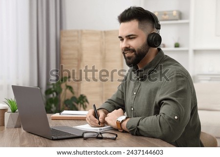 E-learning. Young man taking notes during online lesson at wooden table indoors