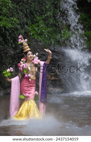 Thai traditional dress fashion show. Beautiful Asian woman portrait dressed in lotus flowers traditional Thai dress at the waterfall. According to her concept in the literature of ancient Thailand.