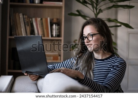 Young female freelancer working from home, sitting comfortably on her couch in the living room.
