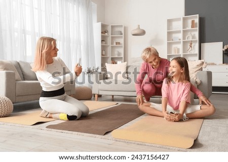 Sporty young woman taking picture of her mother and little daughter training at home