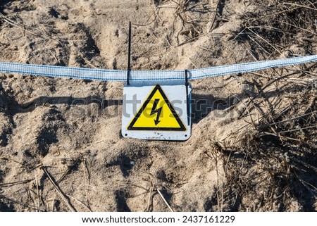 Cautionary Electrical Hazard Sign Placed on Sandy Ground.