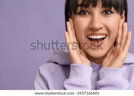 Happy stylish young woman with nose piercing on lilac background