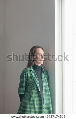 Happy Woman standing next to the window and smiling. Waiting for an addition. Good pregnancy. Vertical composition Royalty-Free Stock Photo #2437174515
