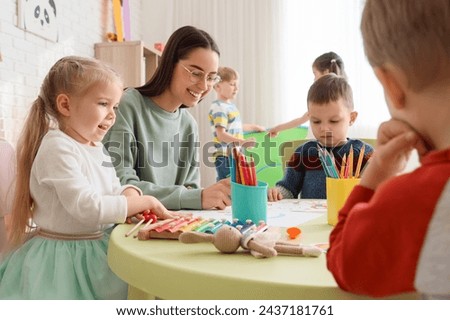 Cute little children with nursery teacher drawing at table in kindergarten Royalty-Free Stock Photo #2437181761