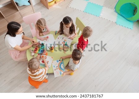 Little children with nursery teacher drawing at table in kindergarten, top view Royalty-Free Stock Photo #2437181767