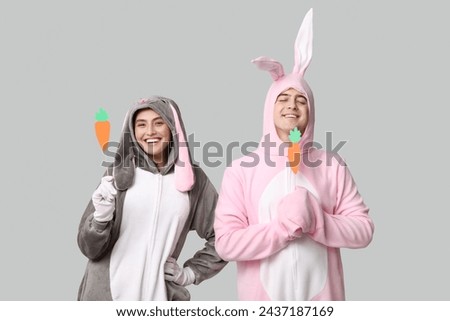 Beautiful young couple in bunny costume with paper carrots on grey background. Easter celebration
