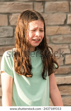 An unexpected dousing from a water mist leaves the little girl feeling a bit disheartened on a warm summer day. Royalty-Free Stock Photo #2437189313