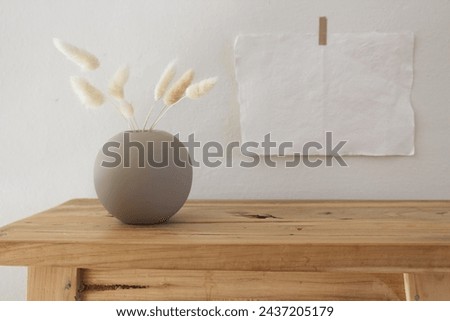 Empty paper sheets and posters mockups taped on a white wall. Wooden bench, table. Modern white ceramic vase with dry Lagurus ovatus grass and cup coffee. Scandinavian interior. Selective focus.     