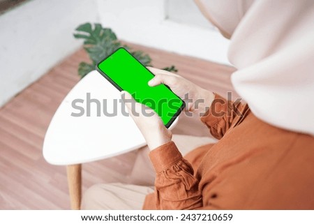 Girl in the room holding a smartphone with a green screen, with a table beside her