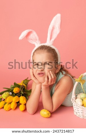 Portrait of cute smiling girl with Bunny ears and yellow Easter eggs, near yellow tulips, isolated on pink background. Happy Easter