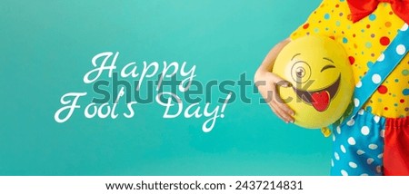 A bright yellow ball with a cheerful face in the hands of a clown child. Birthday and 1 April Fool's day concept.