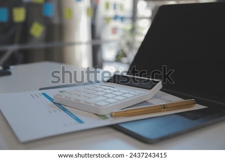 Close up view of simple workspace with laptop, notebooks, coffee cup and tree pot on white table with blurred office room background