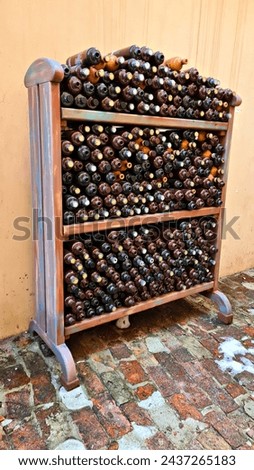 Many ceramic empty bottles for alcoholic drink balsam are stacked in wooden cabinet.