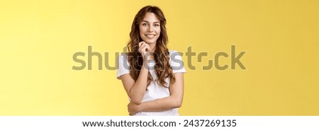 Intrigued attractive european brunette curly long hair look interested listen curious suggestion touch cheek interest temptation smiling toothy pleased good conversation stand yellow background. Royalty-Free Stock Photo #2437269135