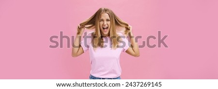 Portrait of pissed outraged and irritated woman losing temper feeling pressured screaming from distress pulling hair out of head standing annoyed over pink background fed up doing haircut every day Royalty-Free Stock Photo #2437269145