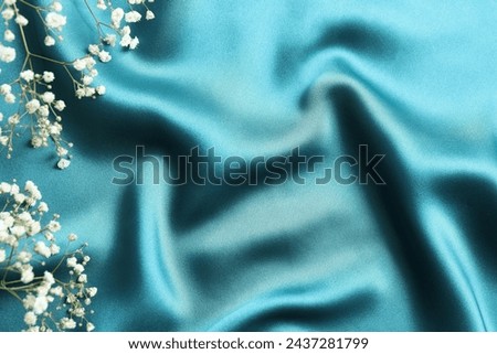 Silk satin dark turquoise color. Shiny smooth fabric with gypsophila. Soft folds. Luxury background with space for design. Flat table, top view
