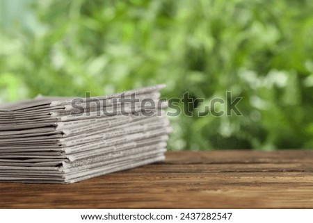 Stack of newspapers on wooden table against blurred green background, space for text. Journalist's work