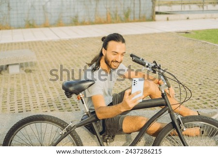 young latin man taking a selfie for his social networks sitting on a bench next to his bike